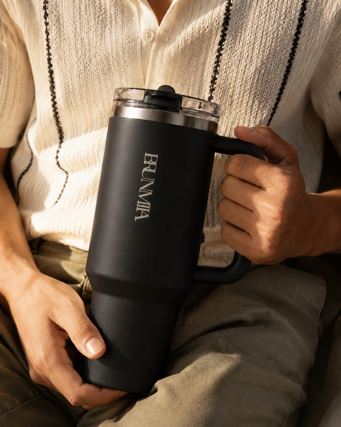 Person holding a black BRUNMIIA handled tumbler in warm indoor light