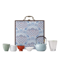Portable ceramic tea set with four assorted cups, glass pitcher, pale blue teapot and blue wave-pattern hard case