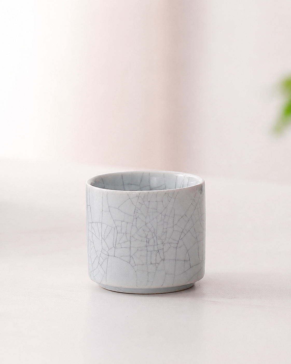 Pale cylindrical ceramic tea cup with decorative crackle-pattern glaze