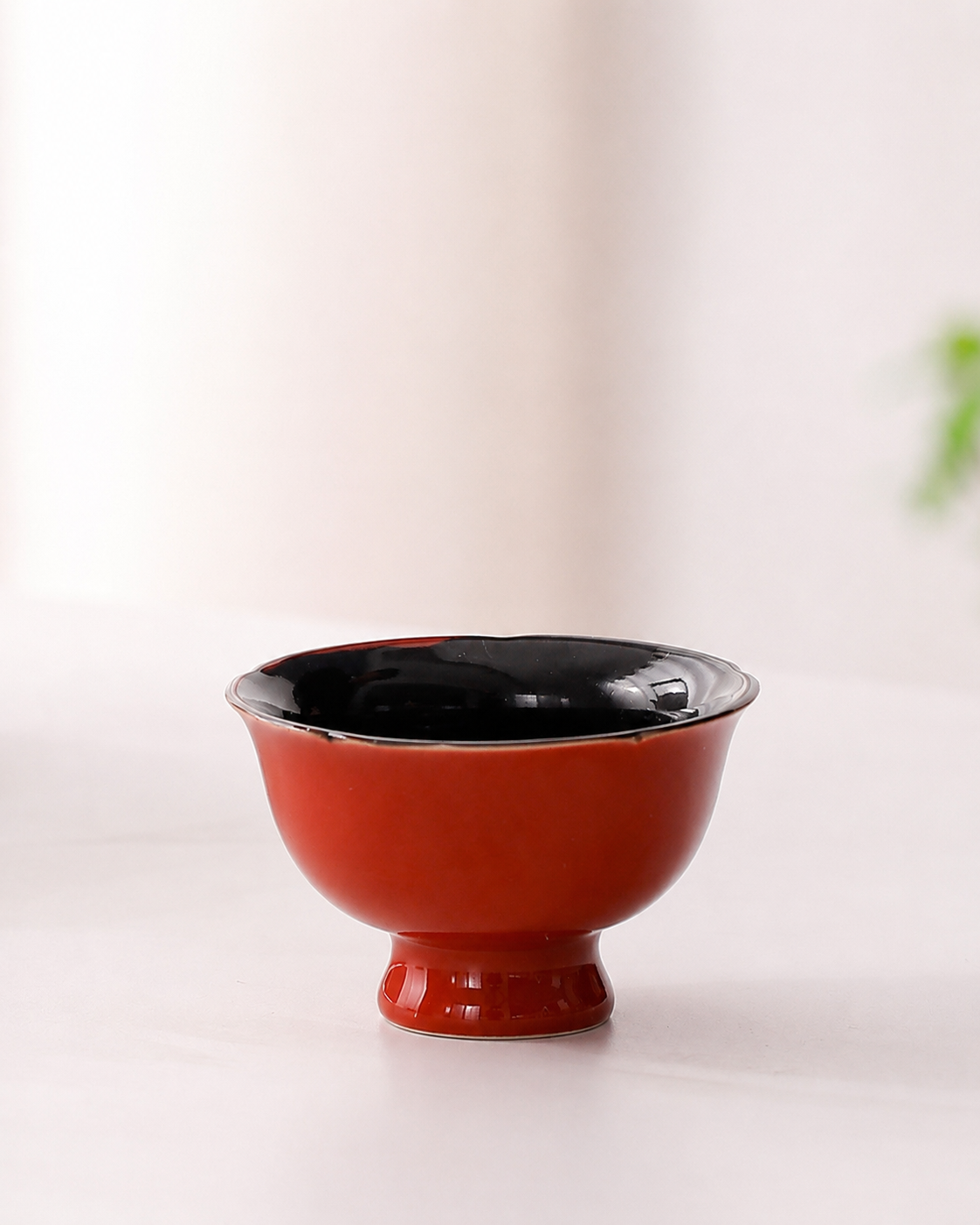 Red footed ceramic tea cup with glossy black interior and shaped rim