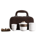 White ceramic travel tea set with teapot, three cups, lidded container, accessory wrap and brown carry case