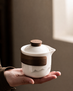 Hand holding the compact white ceramic teapot with mountain pattern and brown-toned details