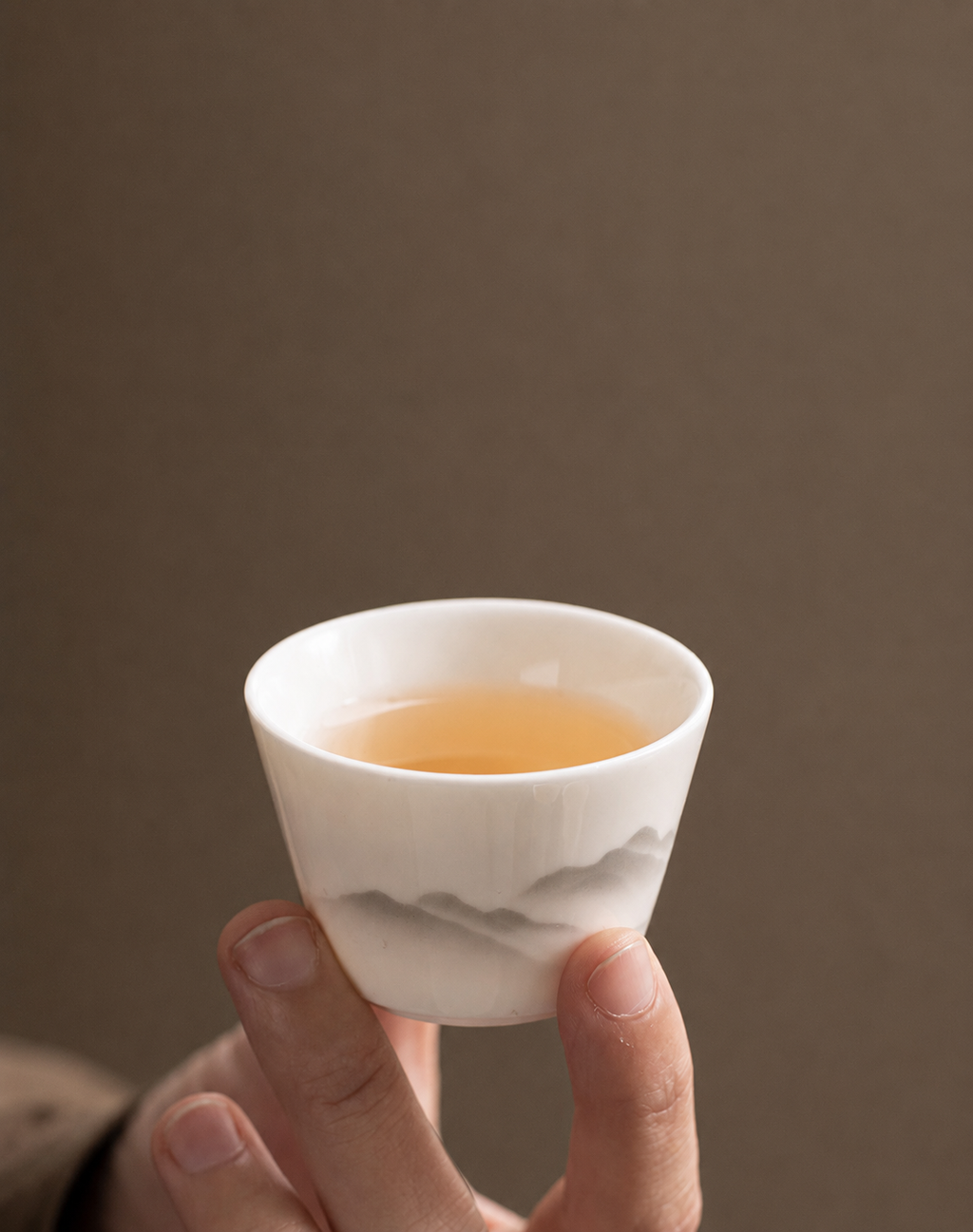 Hand holding a white ceramic tea cup with grey mountain landscape pattern