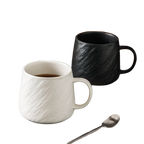 Black stone-texture ceramic mug filled with coffee beside white mug and teaspoon