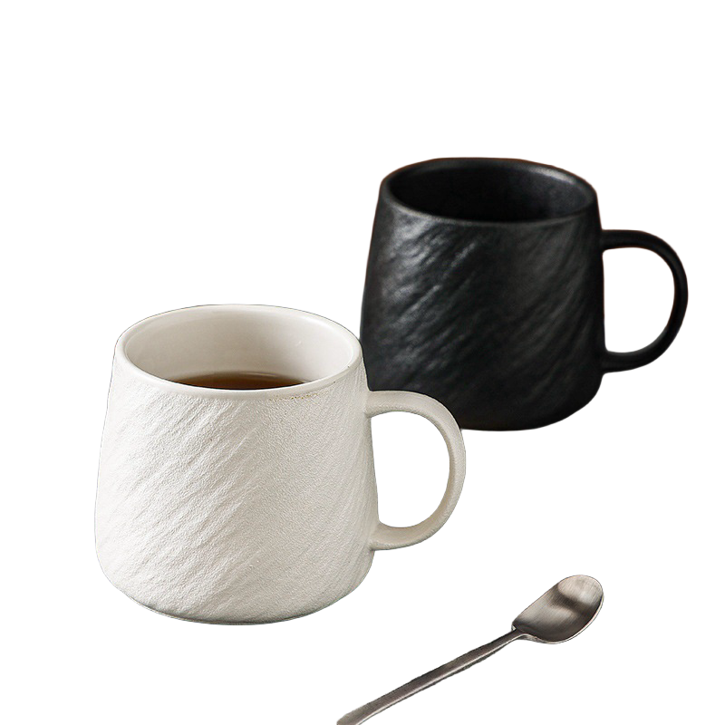 Black stone-texture ceramic mug filled with coffee beside white mug and teaspoon